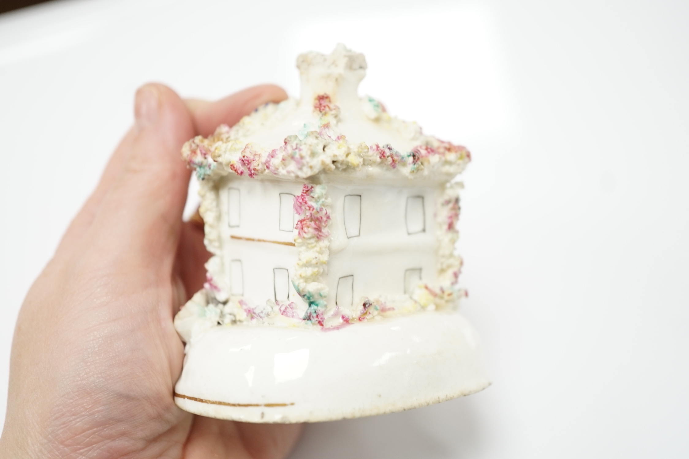 Three Staffordshire porcelain dog figures, c.1830-50, comprising a boy clinging to the back of a spaniel, a model of a poodle with a bird in its mouth and a model of a cottage with a small dog in the doorway, tallest 9cm